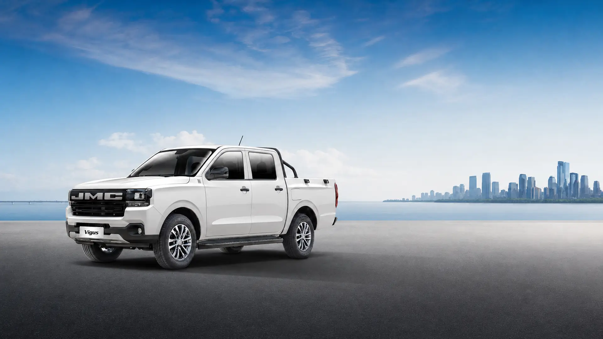Pick-up JMC Vigus double cabine blanc devant une skyline urbaine au bord de l'eau